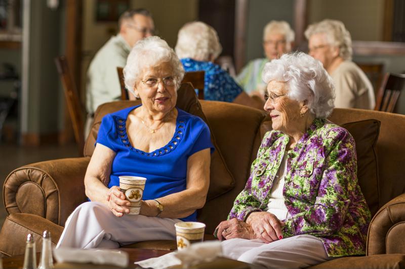 Two senior women drinking coffee on couch.