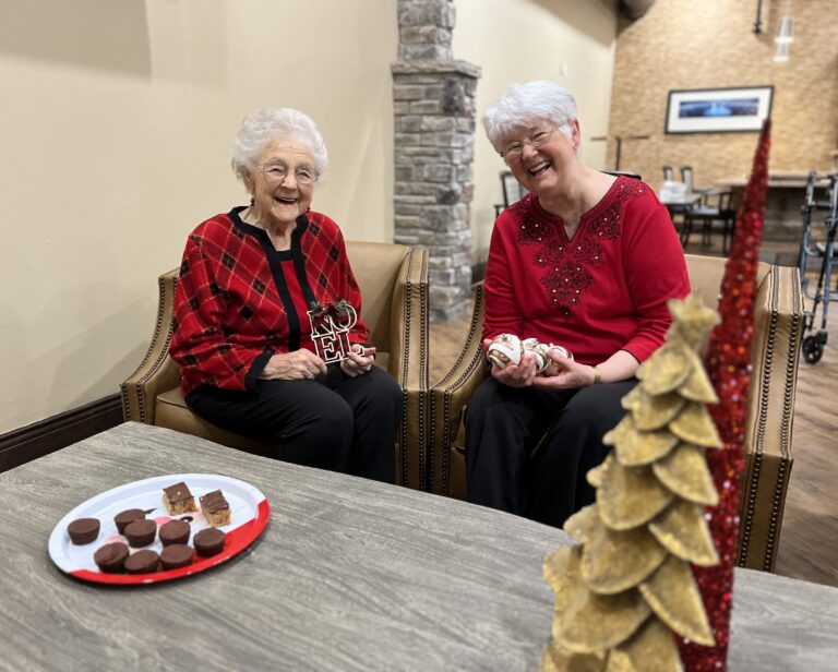 Two senior female residents looking merry in red holiday sweaters