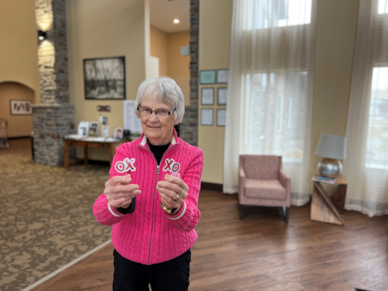 senior female wearing a pink sweater holding xo signs in each hand.